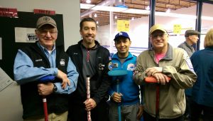 4 men stand together in a curling club.